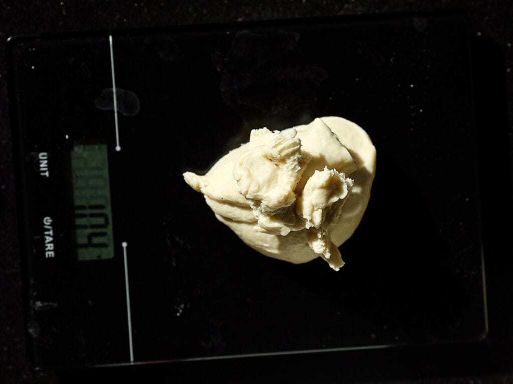 Dough ball resting on a digital kitchen scale displaying weight in a dimly lit setting.